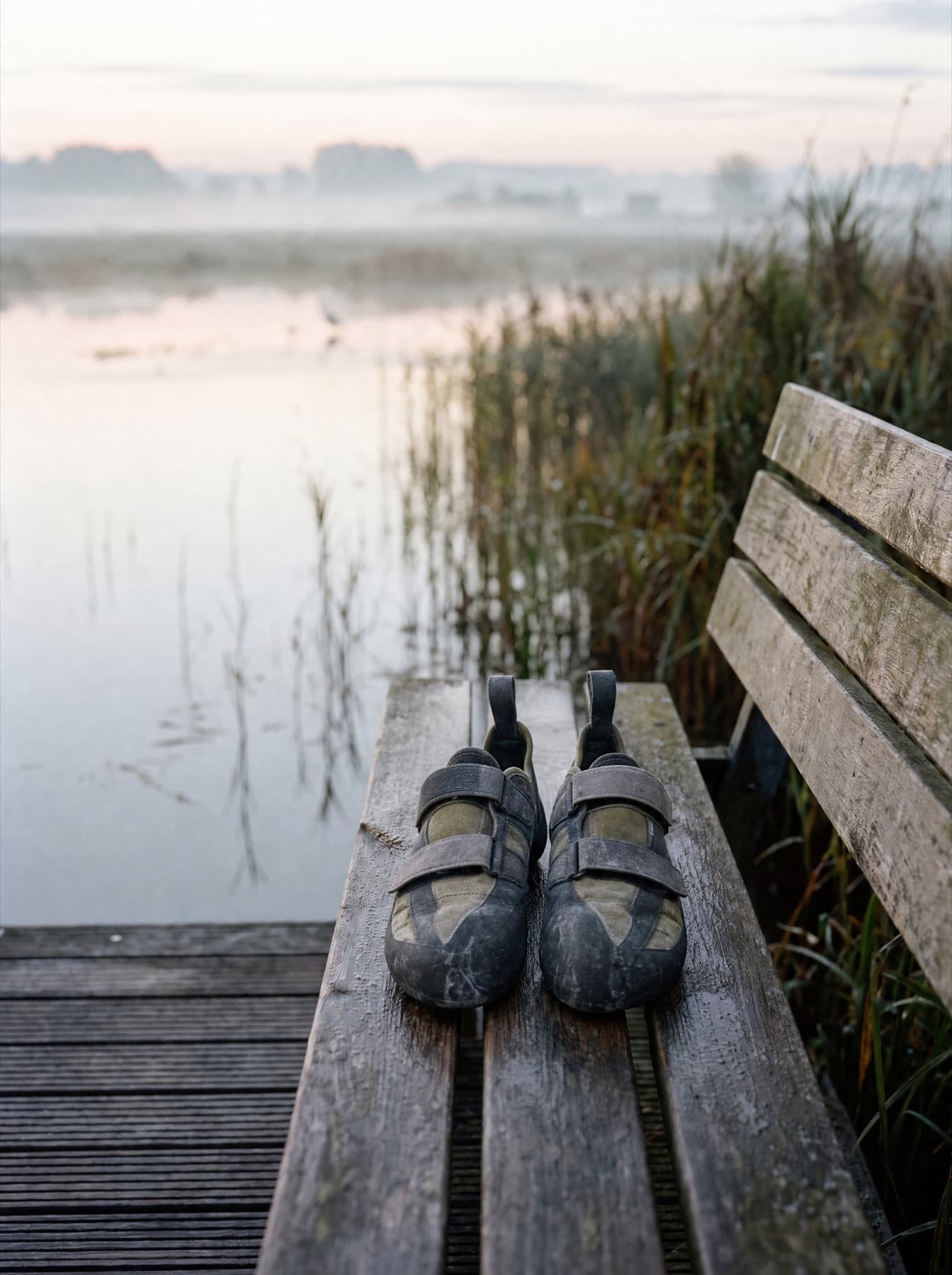 Een paar klimschoenen op een houten bank aan het water, in de ochtendnevel